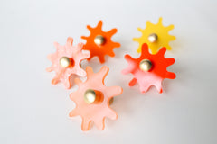 Multiple Splat drawer pulls in various finishes like orange, orange pearl, and yellow orange arranged on a white background, showcasing their versatility and playful character.
