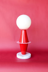 The Totem Lamp by Sazerac Stitches combines bold geometric shapes with Bauhaus-inspired design. Crafted from powder-coated steel in vibrant red and pink hues, it features a frosted globe and sleek marble base.
