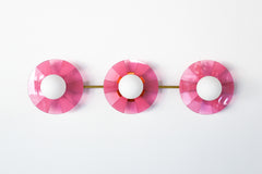 Infuse your space with playful energy with the Fuchsia Fever Triple Circus Sconce. This pink light fixture features three intricately etched acrylic discs, each casting a captivating dance of light and shadow on your walls.