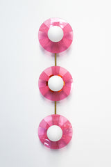 Infuse your space with playful energy with the Fuchsia Fever Triple Circus Sconce. This pink light fixture features three intricately etched acrylic discs, each casting a captivating dance of light and shadow on your walls.