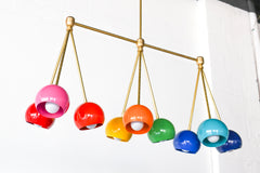 Brightly colored rainbow chandelier fixture with candy colored shades, brass hardware, and a long linear shape.  Beautiful and colorful statement lighting. Bright Rainbow Turmalina Chandelier by Sazerac Stitches - angled side view