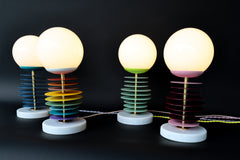 The Vertebrale lamp by Sazerac Stitches combines color, form, and functionality. Powder-coated steel discs in bold hues, a glowing frosted globe, and a sleek marble base create a striking modern design ideal for any interior.