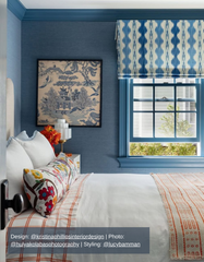 Cozy Nantucket-inspired guest bedroom with deep blue textured walls, custom blue window trim, and a patterned Roman shade, featuring a vibrant mix of textiles including an orange grid duvet, embroidered floral accent pillow, and framed chinoiserie artwork, creating a welcoming coastal aesthetic.