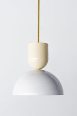 Close-up of the Taeuber Pendant in cream and white by Sazerac Stitches, featuring a glossy two-tone powder-coated finish and brass downrod. This sculptural pendant light showcases minimalist curves and handcrafted detailing, blending midcentury modern design with a soft, neutral palette. Perfect for kitchens, dining rooms, or entryways, this artisan-made fixture adds a timeless and elegant touch to both contemporary and classic interiors.