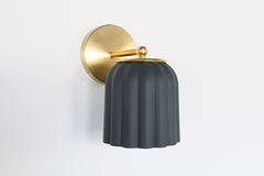 Marcella wall sconce with unglazed matte black ceramic shade and brushed brass backplate, shown on a neutral background. The scalloped silhouette and soft finish evoke timeless elegance with a modern edge, perfect for moody interiors, modern traditional decor, or eclectic spaces seeking contrast and sophistication.