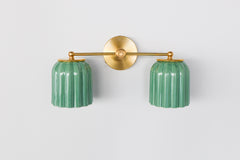 This handcrafted double sconce from Sazerac Stitches combines ribbed ceramic shades in jade green with brass accents, delivering character and elegance to any space.