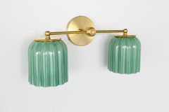 Showcase artisanal craftsmanship with this Sazerac Stitches fixture. The Double Marcella Sconce features jade green ceramic shades and a brass base, perfect for interiors seeking unique design.