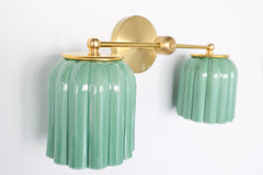 The Double Marcella Sconce is a bathroom-ready light with jade green ribbed shades and brass accents. Perfect above a mirror or vanity for stylish, functional illumination.