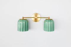 This handcrafted double sconce from Sazerac Stitches combines ribbed ceramic shades in jade green with brass accents, delivering character and elegance to any space.