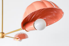 The Coquille Chandelier shown in a soft peach finish features three sculptural shell-shaped shades with white globe bulbs, mounted on a sleek brass three-arm structure. Suspended from a central brass rod, this ceiling fixture blends Art Deco elegance with whimsical, beach-inspired charm. The pastel tone and playful curves make it ideal for eclectic, coastal, or vintage-inspired spaces like dining rooms, nurseries, or boutique retail environments.