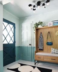 Colorblocked entryway with white and teal walls, graphic black and white rug, modern wood bench with hooks, and a zodiac instpired flushmount ceiling light made by Sazerac Stitches in a matte black finish