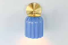 Marcella ceramic wall sconce in glazed sky blue with a fluted shade and brushed brass backplate, shown against a light gray background. This handcrafted fixture blends playful vintage style with modern sophistication, ideal for traditional, preppy, or coastal interiors seeking a pop of cheerful blue and timeless silhouette.