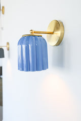 Marcella ceramic wall sconce in glazed sky blue with a fluted shade and brushed brass backplate, shown against a light gray background. This handcrafted fixture blends playful vintage style with modern sophistication, ideal for traditional, preppy, or coastal interiors seeking a pop of cheerful blue and timeless silhouette.
