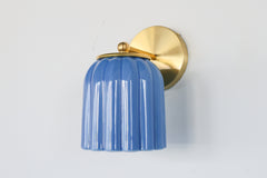 Marcella ceramic wall sconce in glazed sky blue with a fluted shade and brushed brass backplate, shown against a light gray background. This handcrafted fixture blends playful vintage style with modern sophistication, ideal for traditional, preppy, or coastal interiors seeking a pop of cheerful blue and timeless silhouette.