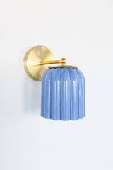 Marcella ceramic wall sconce in glazed sky blue with a fluted shade and brushed brass backplate, shown against a light gray background. This handcrafted fixture blends playful vintage style with modern sophistication, ideal for traditional, preppy, or coastal interiors seeking a pop of cheerful blue and timeless silhouette.