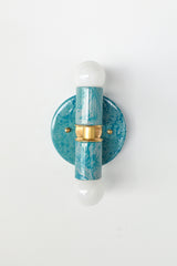 A handcrafted Teal and Grey Marbled Thalia Sconce with dual bulbs, shown against a white wall. The fixture features swirling marbled enamel in soft teal and grey, paired with warm brass hardware. Ideal for modern bathrooms, vanities, or entryways seeking a pop of bold, artistic lighting.