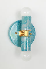 The Thalia Sconce in Teal and Grey Marbled finish is a bold, artistic wall light with two globe bulbs and a circular brass base. Featuring hand-applied marbled enamel in coastal-inspired hues, this sconce is perfect for adding a unique touch to bathroom lighting, powder rooms, or hall spaces.