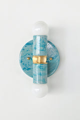 The Thalia Sconce in Teal and Grey Marbled finish is a bold, artistic wall light with two globe bulbs and a circular brass base. Featuring hand-applied marbled enamel in coastal-inspired hues, this sconce is perfect for adding a unique touch to bathroom lighting, powder rooms, or hall spaces.