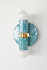 Close-up view of the Teal and Grey Marbled Thalia Sconce, a modern double-bulb wall light featuring hand-marbled teal and grey enamel with solid brass accents. This sculptural lighting fixture blends artistic flair with function, making it a standout in bathrooms, powder rooms, or hallways.