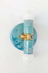 A handcrafted Teal and Grey Marbled Thalia Sconce with dual bulbs, shown against a white wall. The fixture features swirling marbled enamel in soft teal and grey, paired with warm brass hardware. Ideal for modern bathrooms, vanities, or entryways seeking a pop of bold, artistic lighting.