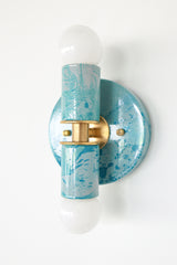 Close-up view of the Teal and Grey Marbled Thalia Sconce, a modern double-bulb wall light featuring hand-marbled teal and grey enamel with solid brass accents. This sculptural lighting fixture blends artistic flair with function, making it a standout in bathrooms, powder rooms, or hallways.