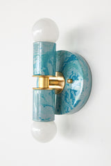 A handcrafted Teal and Grey Marbled Thalia Sconce with dual bulbs, shown against a white wall. The fixture features swirling marbled enamel in soft teal and grey, paired with warm brass hardware. Ideal for modern bathrooms, vanities, or entryways seeking a pop of bold, artistic lighting.