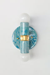 The Thalia Sconce in Teal and Grey Marbled finish is a bold, artistic wall light with two globe bulbs and a circular brass base. Featuring hand-applied marbled enamel in coastal-inspired hues, this sconce is perfect for adding a unique touch to bathroom lighting, powder rooms, or hall spaces.