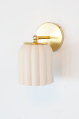 Marcella ceramic wall sconce in unglazed porcelain white with brushed brass hardware, showcasing a fluted, scalloped silhouette. This timeless fixture complements traditional, Southern-inspired, or coastal interiors with its soft matte finish and refined detailing—perfect for powder rooms, bathrooms, or hallways seeking classic charm with a sculptural edge.