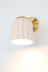 Marcella ceramic wall sconce in unglazed porcelain white with brushed brass hardware, showcasing a fluted, scalloped silhouette. This timeless fixture complements traditional, Southern-inspired, or coastal interiors with its soft matte finish and refined detailing—perfect for powder rooms, bathrooms, or hallways seeking classic charm with a sculptural edge.