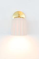 Unglazed white porcelain Marcella sconce with warm brass accents, featuring a fluted ceramic shade and classic rounded backplate. Ideal for transitional interiors, coastal cottages, and Southern-style homes, this handmade light fixture adds refined texture and soft elegance to bathrooms, bedrooms, or hallway vignettes.