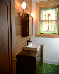 Rustic bathroom with green floral tile, stained glass window, and wood paneling
