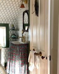 Attic bathroom with wallpaper, dark green trim, a skirted sink with brass hardware, and a small black mirror.  Grandmillenniel vibes that looks beautiful in an older home.