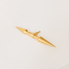 A brass double-ended spike handle from Sazerac Stitches, featuring two symmetrical pointed ends and a central mounting stem. This unique hardware piece has a bold, sculptural design, crafted from solid brass with a smooth, polished finish. Ideal for use as a decorative drawer pull, cabinet handle, or furniture accent, adding an edgy, modern touch to interiors. The warm golden hue of the brass patina enhances its vintage-inspired aesthetic.