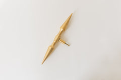 A brass double-ended spike handle from Sazerac Stitches, featuring two symmetrical pointed ends and a central mounting stem. This unique hardware piece has a bold, sculptural design, crafted from solid brass with a smooth, polished finish. Ideal for use as a decorative drawer pull, cabinet handle, or furniture accent, adding an edgy, modern touch to interiors. The warm golden hue of the brass patina enhances its vintage-inspired aesthetic.