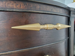 A brass double-ended spike handle from Sazerac Stitches, featuring two symmetrical pointed ends and a central mounting stem. This unique hardware piece has a bold, sculptural design, crafted from solid brass with a smooth, polished finish. Ideal for use as a decorative drawer pull, cabinet handle, or furniture accent, adding an edgy, modern touch to interiors. The warm golden hue of the brass patina enhances its vintage-inspired aesthetic.