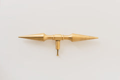 A brass double-ended spike handle from Sazerac Stitches, featuring two symmetrical pointed ends and a central mounting stem. This unique hardware piece has a bold, sculptural design, crafted from solid brass with a smooth, polished finish. Ideal for use as a decorative drawer pull, cabinet handle, or furniture accent, adding an edgy, modern touch to interiors. The warm golden hue of the brass patina enhances its vintage-inspired aesthetic.