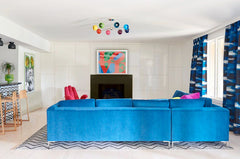 pop arm style living room with rainbow chandelier, blue sofa, and colorful curtains