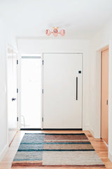 Neutral mid century modern hallway with white walls, natural wood floors, a striped neutral rug, and a flushmount ceiling light fixture in pastel pink and brass