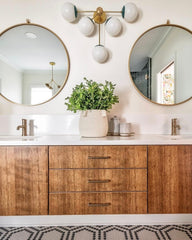 Neutral bathroom design with hexagon penny tile floor, wood cabinet, circular gold mirrors, and and brass hardware