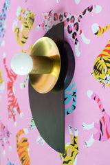A graphic, architectural wall sconce from the Kin collection, shown in a dramatic black and brass colorway. The matte black semicircle backplate creates a bold silhouette against any wall, while the reflective brass shade adds a touch of glamour and warmth. Its Bauhaus-inspired geometry and sleek profile make it a versatile lighting choice—perfect for luxe bedrooms, artful entryways, or moody dining rooms with a sculptural edge. Designed to stand alone or in pairs, this fixture works beautifully in modern,