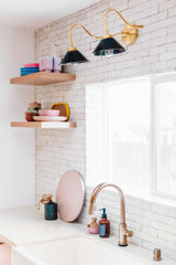 white handmade tile backsplash with wood floating shelves and a brass and black two light wall sconce