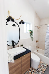 neutral bathroom renovation with a wood and black vanity with a black circular mirror and a black and brass wall sconce