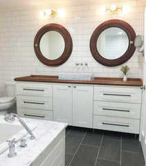 Melpomene sconces above wood mirrors on a subway tile wall