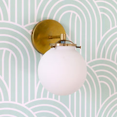 Brass wall sconce with white glass on a mint and white art deco inspired wallpaper