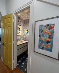 Seen through a yellow doorway, this playful powder room showcases a Kin Sconce glowing beside a modern mirror. With patterned tile floors, swirled navy wallpaper, and a floating vanity, the space perfectly illustrates how our colorful geometric sconces can bring charm, contrast, and function to design-forward bathrooms.