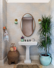 Neutral coastal style bathroom with a textural wallpaper in a metallic starburst pattern with a textural houseplant, rattan side table, linen handtowels, mint accents, natural wood mirror, and two brass and mint wall sconces in a curvy globe shade.  Colorful coastal traditional home decor style.