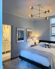 light blue bedroom with modern brass floral chandelier over a simple bedframe.  Bedroom decorated with matisse posters.