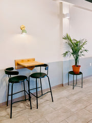 Restaurant design featuring a color blocked stripe on the wall, natural wood bistro-height table with two black stools.  Above the table is a brass and mint wall sconce by sazerac stitches.