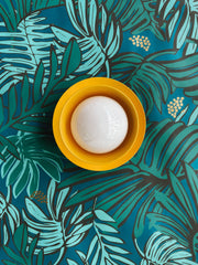 mustard wall sconce on a botanical themed wallpaper that is shades of green, teal, and mint