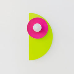 The neon Kin Sconce in chartreuse, doll pink, and orange, featuring a sculptural half-circle backplate and circular shade with a central bulb. This wall sconce channels bold Memphis Group energy with Bauhaus-inspired geometry and saturated color blocking—perfect for playful interiors, maximalist spaces, kids' rooms, or modern art-forward homes that embrace high-impact, unconventional design.